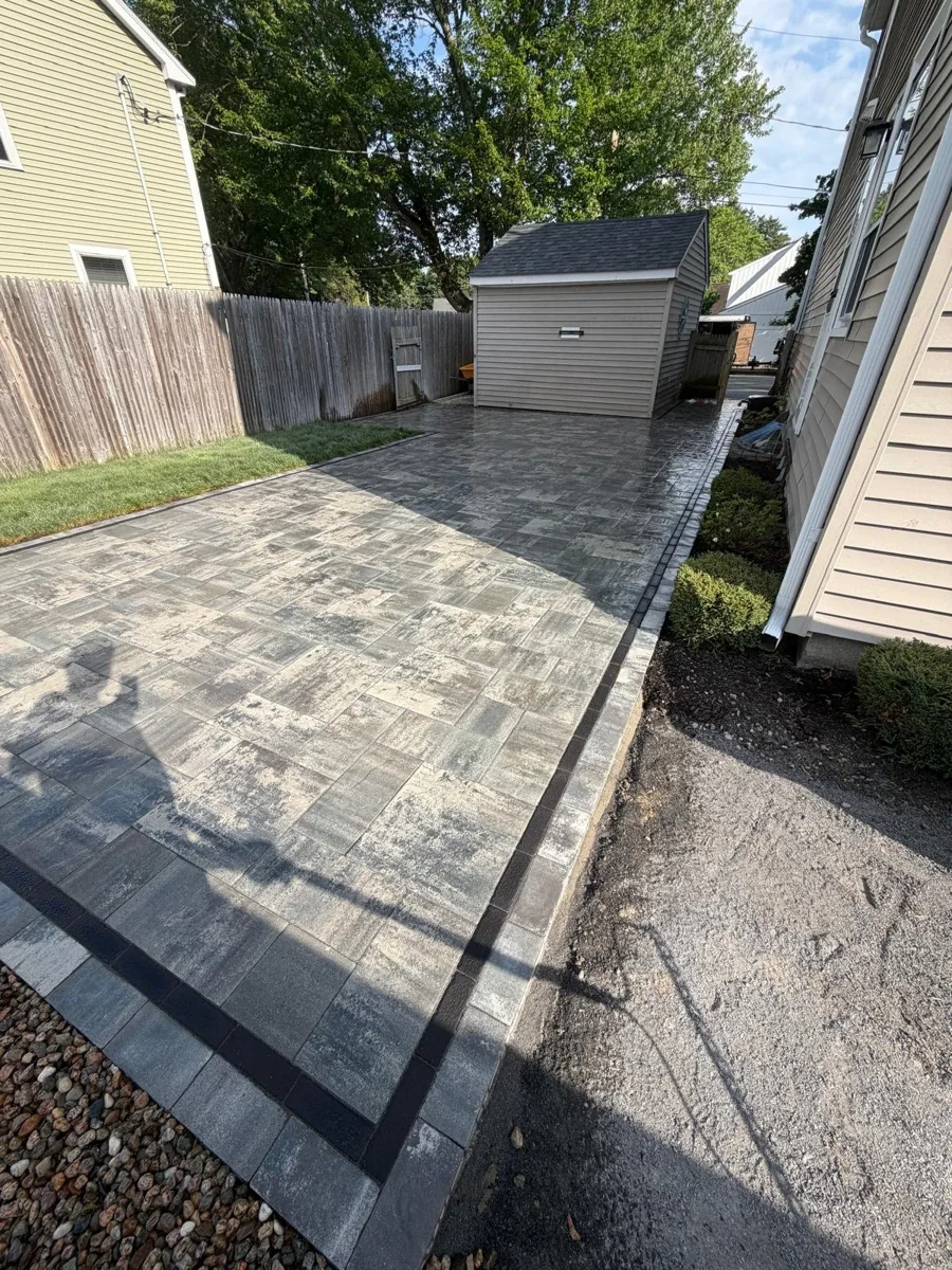 Rectangular gray paver patio with a dark border beside a house
